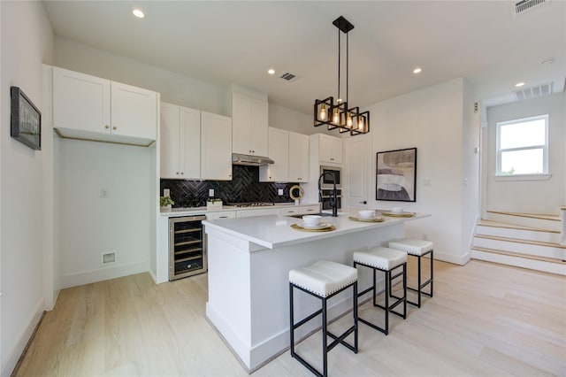 2312 Reinerman St, Houston, TX 77007 - kitchen with wine cooler, light wood finished floors, decorative backsplash, white cabinets, and an island with sink