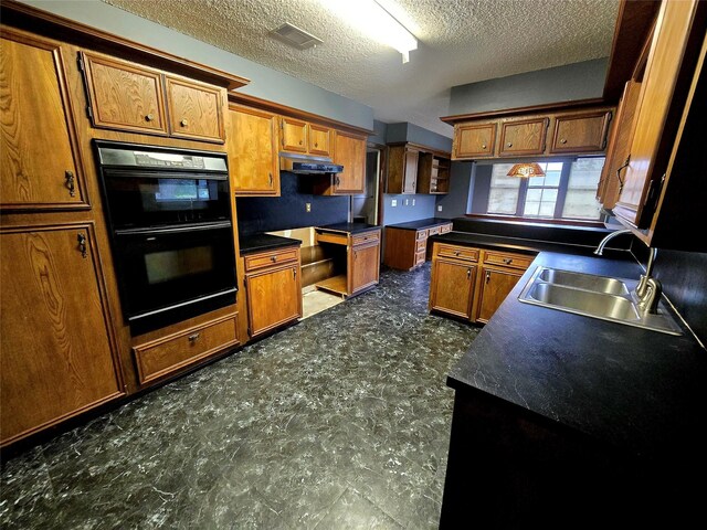 5000 Magnolia Ln, Bay City, TX 77414 - kitchen featuring under cabinet range hood, brown cabinetry, a sink, and a textured ceiling