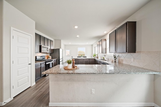 5330 Briana Dee Dr, Rosharon, TX 77583 - kitchen featuring appliances with stainless steel finishes, a peninsula, dark brown cabinets, dark wood-style flooring, and light stone counters