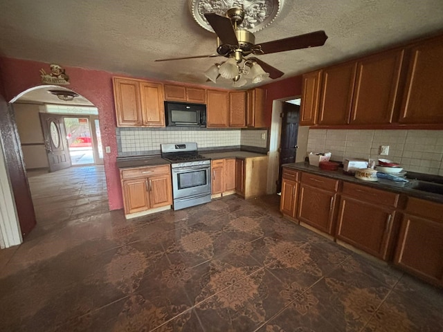 1205 14th St, Seagraves, TX 79359 - kitchen featuring stainless steel range with gas stovetop, black microwave, decorative backsplash, dark countertops, and arched walkways