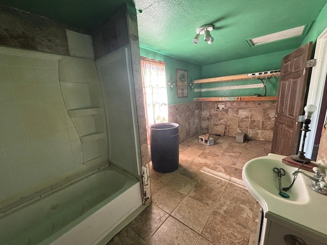 1205 14th St, Seagraves, TX 79359 - full bath featuring tile walls, a wainscoted wall, shower / bathtub combination, a textured ceiling, and stone finish floors