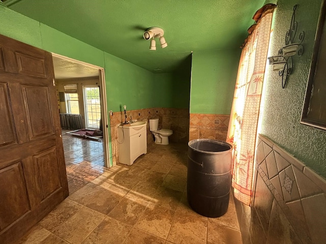 1205 14th St, Seagraves, TX 79359 - bathroom with a wainscoted wall, toilet, a sink, tile walls, and a textured ceiling