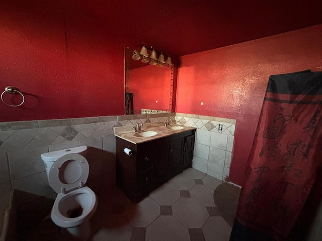 1205 14th St, Seagraves, TX 79359 - full bathroom featuring tile walls, toilet, double vanity, a wainscoted wall, and tile patterned flooring