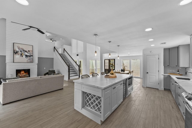 1323 Warwickshire Dr, Houston, TX 77077 - kitchen featuring gray cabinetry, a sink, light stone countertops, a fireplace, and light wood finished floors