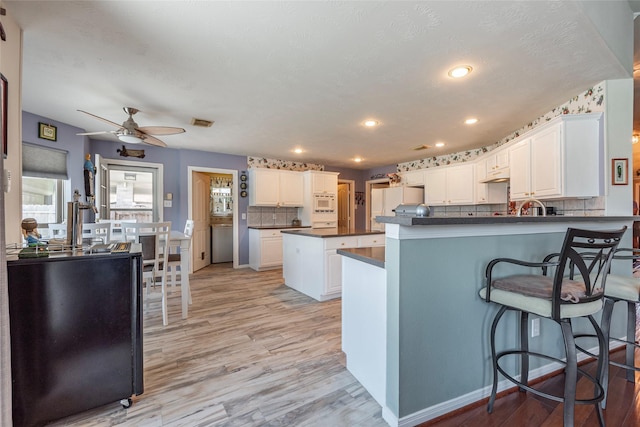 811 Hackberry Ln, Friendswood, TX 77546 - kitchen with dark countertops, a peninsula, light wood finished floors, white appliances, and a ceiling fan