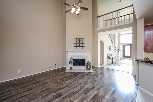 2803 Lakecrest Way Dr, Katy, TX 77493 - unfurnished living room featuring ceiling fan, arched walkways, dark wood-style flooring, a high ceiling, and a fireplace with flush hearth