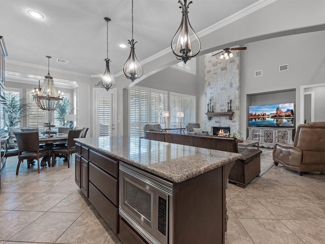 12118 Pinelands Park Ln, Humble, TX 77346 - kitchen with stainless steel microwave, ornamental molding, a fireplace, a chandelier, and dark brown cabinetry