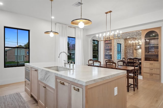 3111 Eastman St, Houston, TX 77022 - kitchen featuring a sink, light wood-type flooring, a kitchen island with sink, light brown cabinets, and hanging light fixtures
