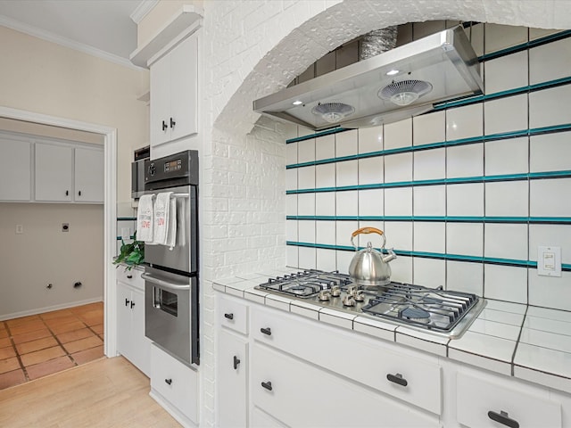 1735 Hodge Lake Ln, Sugar Land, TX 77478 - kitchen featuring tile counters, range hood, appliances with stainless steel finishes, white cabinetry, and ornamental molding