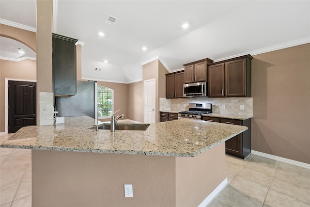 18934 Sorrento Point Dr, New Caney, TX 77357 - kitchen featuring stainless steel appliances, a sink, arched walkways, dark brown cabinetry, and light stone countertops