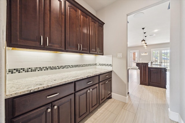 10306 Grape Creek Grove Ln, Cypress, TX 77433 - kitchen featuring backsplash, dark brown cabinetry, light stone countertops, and baseboards