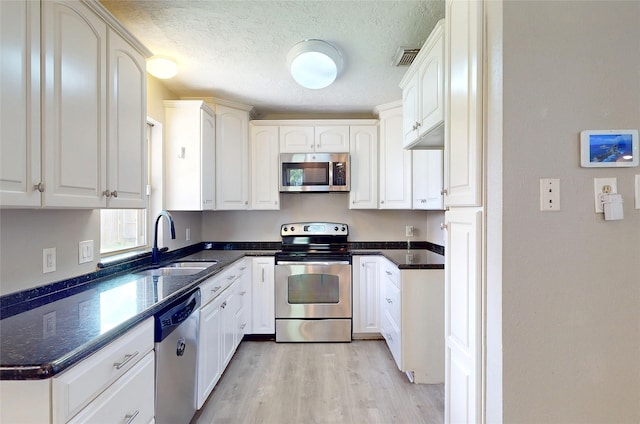 3907 Texas Ave, Dickinson, TX 77539 - kitchen featuring appliances with stainless steel finishes, a sink, light wood finished floors, white cabinetry, and a textured ceiling