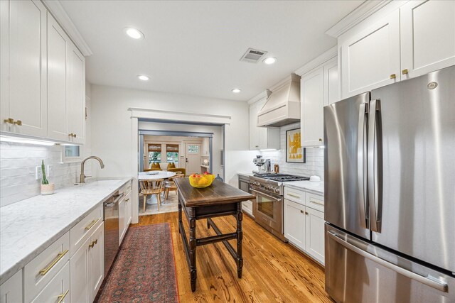 1336 Tulane St, Houston, TX 77008 - kitchen with appliances with stainless steel finishes, custom range hood, light wood finished floors, a sink, and white cabinets