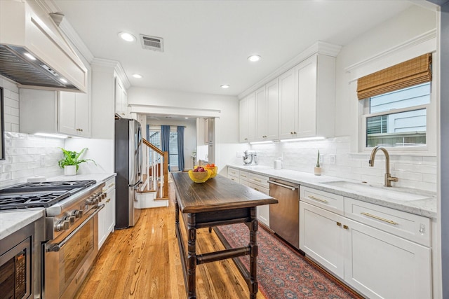 1336 Tulane St, Houston, TX 77008 - kitchen with stainless steel appliances, custom exhaust hood, white cabinets, a sink, and light wood finished floors