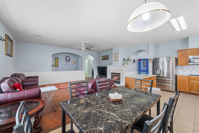 16310 Autumn Leigh Dr, Houston, TX 77083 - dining space featuring arched walkways, a glass covered fireplace, a ceiling fan, and light tile patterned flooring