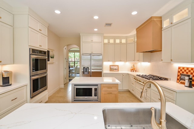 4511 Wickby St, Fulshear, TX 77441 - kitchen with stainless steel appliances, arched walkways, light tile patterned flooring, recessed lighting, and glass insert cabinets