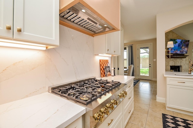4511 Wickby St, Fulshear, TX 77441 - kitchen with exhaust hood, stainless steel gas cooktop, white cabinetry, light stone countertops, and light tile patterned floors