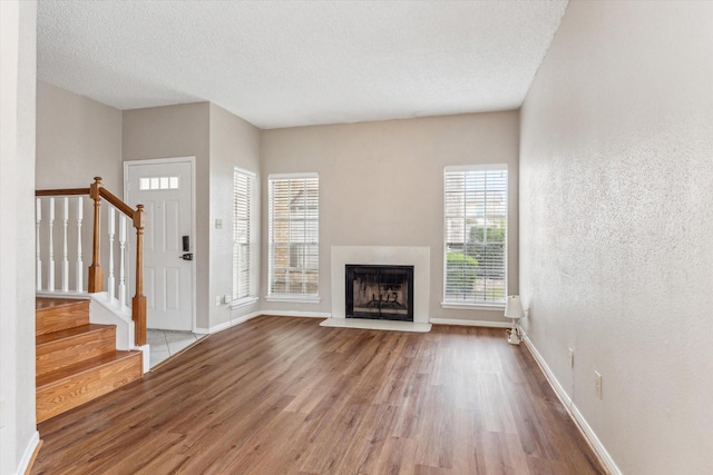 7575 Cambridge St Unit 1906, Houston, TX 77054 - unfurnished living room featuring wood finished floors, stairway, baseboards, a fireplace with raised hearth, and a textured ceiling