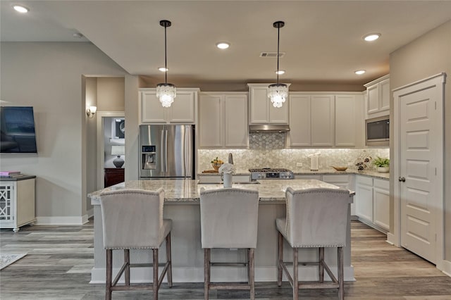 127 Kingsley Grove St, Montgomery, TX 77316 - kitchen featuring stainless steel appliances, under cabinet range hood, decorative backsplash, white cabinetry, and an island with sink