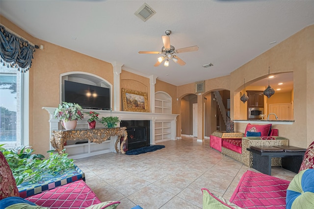 7207 Alder Springs Ct, Katy, TX 77494 - living area with arched walkways, a ceiling fan, light tile patterned floors, a fireplace with raised hearth, and built in shelves