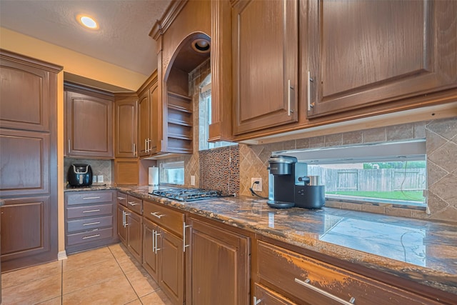 7207 Alder Springs Ct, Katy, TX 77494 - kitchen featuring decorative backsplash, dark stone counters, light tile patterned floors, stainless steel gas cooktop, and a textured ceiling