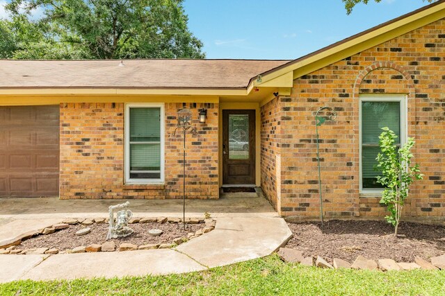 104 Meadowlark Ln, Angleton, TX 77515 - doorway to property with brick siding, a shingled roof, and a garage
