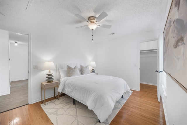10310 Minturn Ln, Houston, TX 77064 - bedroom with light wood finished floors, a textured ceiling, baseboards, a ceiling fan, and a walk in closet