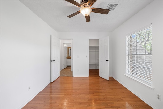 10310 Minturn Ln, Houston, TX 77064 - unfurnished bedroom featuring light wood finished floors, a textured ceiling, baseboards, a walk in closet, and a ceiling fan