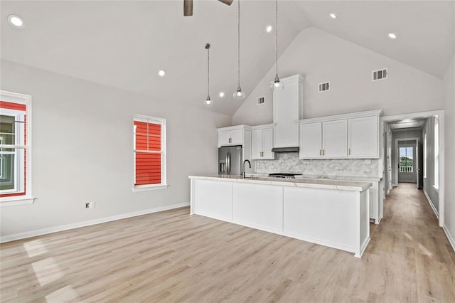 1104 62nd St, Galveston, TX 77551 - kitchen featuring stainless steel fridge, white cabinets, light countertops, an island with sink, and high vaulted ceiling