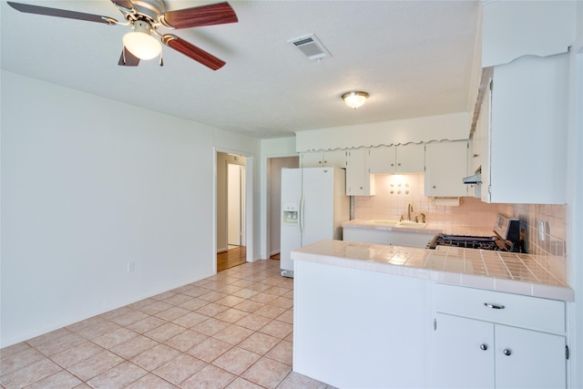 705 Kalmer St, Pasadena, TX 77502 - kitchen featuring gas range, white refrigerator with ice dispenser, tile counters, tasteful backsplash, and a peninsula