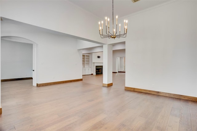 13502 Winter Creek Ct, Houston, TX 77077 - unfurnished living room featuring baseboards, light wood finished floors, arched walkways, built in shelves, and a high ceiling