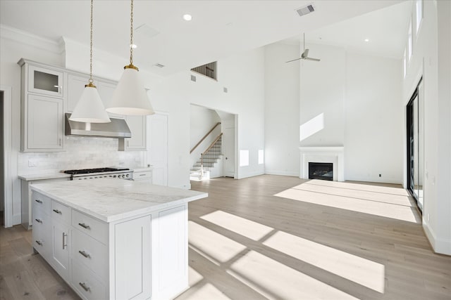 1139 Castellina Ln, Houston, TX 77055 - kitchen featuring wall chimney exhaust hood, a high ceiling, decorative backsplash, open floor plan, and light wood-type flooring