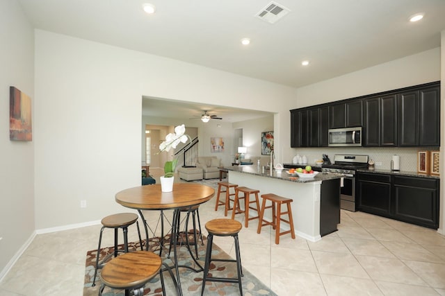 24710 Royal Pike Dr, Katy, TX 77493 - kitchen with appliances with stainless steel finishes, dark cabinetry, a kitchen island with sink, light tile patterned floors, and a breakfast bar