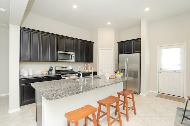 24710 Royal Pike Dr, Katy, TX 77493 - kitchen featuring appliances with stainless steel finishes, a sink, light tile patterned flooring, light stone counters, and an island with sink