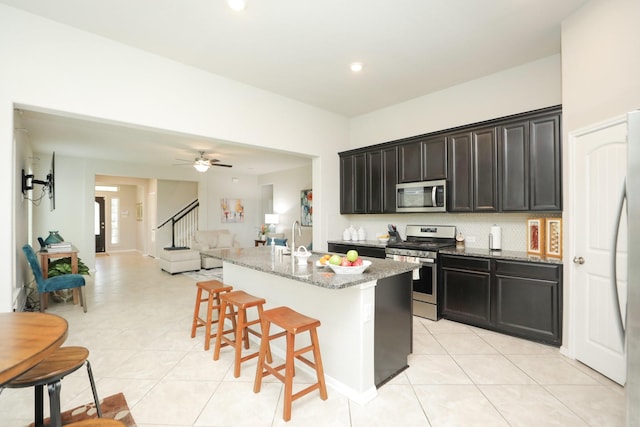 24710 Royal Pike Dr, Katy, TX 77493 - kitchen featuring appliances with stainless steel finishes, light tile patterned floors, a kitchen island with sink, a breakfast bar, and light stone countertops