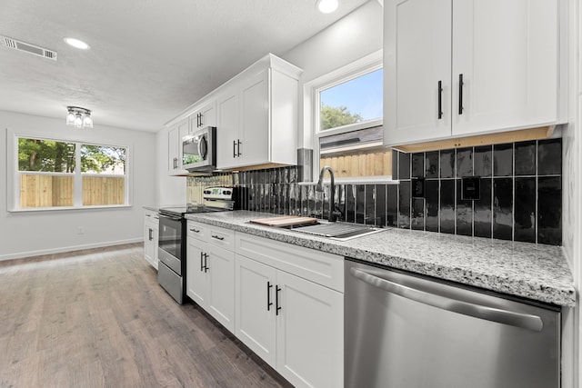 7414 Sunlight Ln, Houston, TX 77095 - kitchen featuring appliances with stainless steel finishes, a sink, white cabinetry, wood finished floors, and healthy amount of natural light
