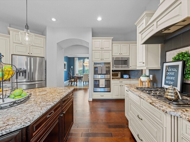 17611 Bear River Ln, Humble, TX 77346 - kitchen with appliances with stainless steel finishes, arched walkways, custom exhaust hood, light stone countertops, and tasteful backsplash