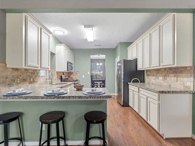 3106 Lake Breeze Ln, Crosby, TX 77532 - kitchen with stainless steel appliances, a sink, a peninsula, a breakfast bar, and a textured ceiling
