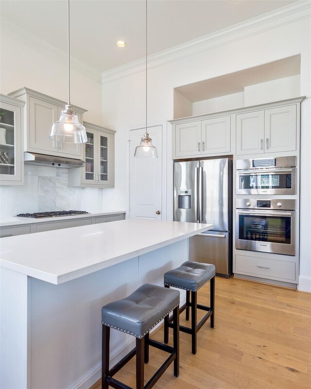 2745 Providence St, Houston, TX 77020 - kitchen with appliances with stainless steel finishes, crown molding, under cabinet range hood, light wood finished floors, and decorative backsplash