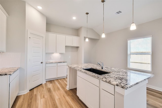 1203 Wildflower Way Dr, Beasley, TX 77417 - kitchen featuring light wood-type flooring, white cabinetry, vaulted ceiling, light stone counters, and decorative light fixtures