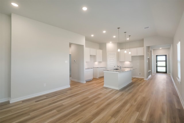 1203 Wildflower Way Dr, Beasley, TX 77417 - kitchen featuring white cabinets, light wood finished floors, a center island with sink, vaulted ceiling, and light stone counters