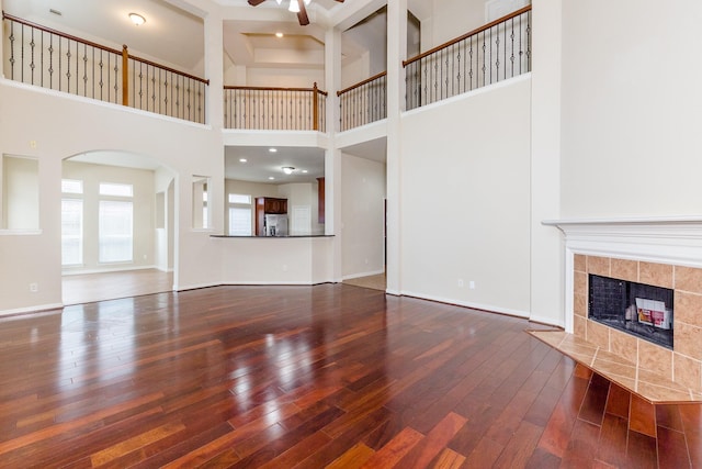 3531 Urban Woods Trl, Houston, TX 77008 - unfurnished living room featuring ceiling fan, hardwood / wood-style flooring, a towering ceiling, a tile fireplace, and arched walkways