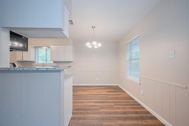 9003 Chateau Forest Dr, Houston, TX 77088 - kitchen with a chandelier, white cabinetry, wood finished floors, a wainscoted wall, and decorative light fixtures