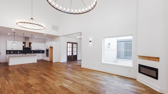 4785 W Fork Blvd, Conroe, TX 77304 - unfurnished living room featuring a chandelier, a glass covered fireplace, light wood-style flooring, a high ceiling, and baseboards