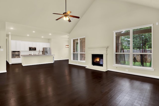 12406 Fort Isabella Ct, Tomball, TX 77375 - unfurnished living room featuring high vaulted ceiling, a ceiling fan, a glass covered fireplace, dark wood-type flooring, and baseboards