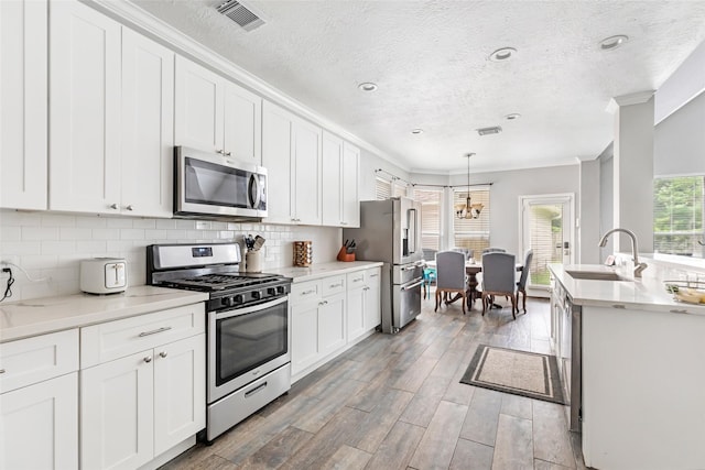 2907 Silverberry Trl, Houston, TX 77345 - kitchen featuring appliances with stainless steel finishes, a sink, crown molding, white cabinetry, and light wood finished floors