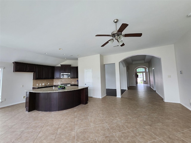 13705 Rainwater Dr, Pearland, TX 77584 - kitchen with decorative backsplash, arched walkways, a center island with sink, ceiling fan, and open floor plan