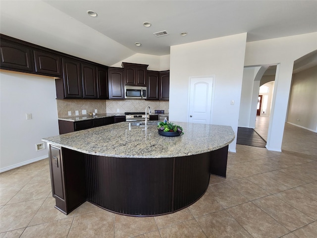 13705 Rainwater Dr, Pearland, TX 77584 - kitchen with stainless steel microwave, arched walkways, light stone counters, tasteful backsplash, and light tile patterned floors
