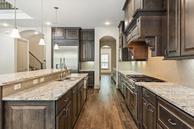 12710 Pebblebrook Dr, Houston, TX 77024 - kitchen featuring arched walkways, a sink, high end appliances, dark wood-style floors, and dark brown cabinets