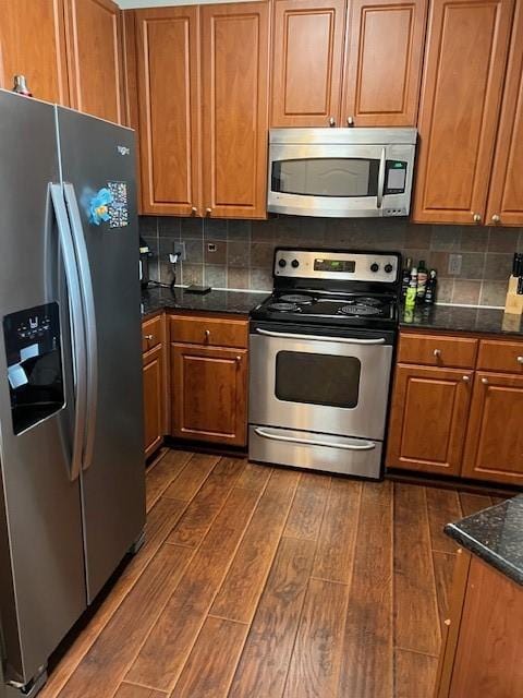 1711 Old Spanish Trl Unit 313, Houston, TX 77054 - kitchen with appliances with stainless steel finishes, dark wood-style flooring, brown cabinetry, tasteful backsplash, and dark stone countertops